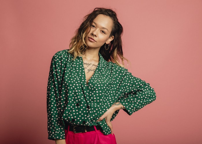 Goodwill AZ | Woman wearing a dark grean and white polkadot top against a coral colored background