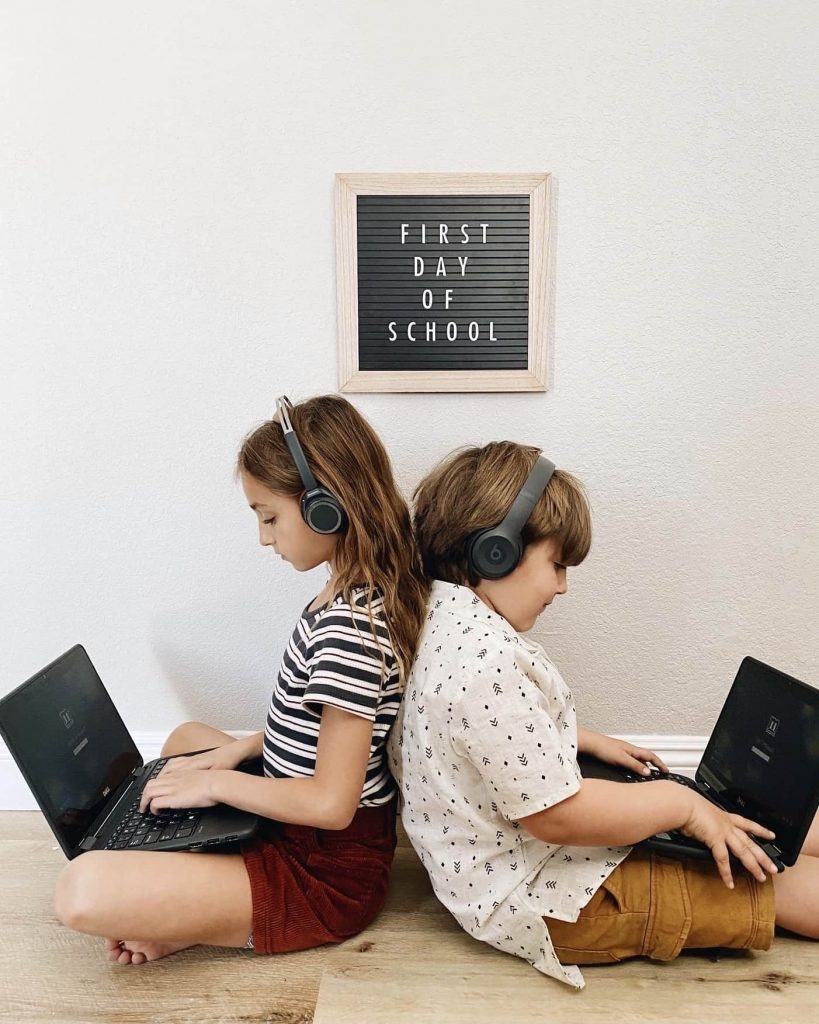 Goodwill AZ | Children sitting back-to-back wearing headphones on laptops underneath a first day of school sign