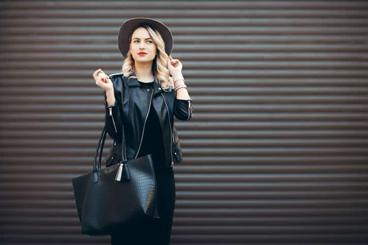 Goodwill AZ | Street portrait of young stylish lady wearing trendy fall outfit. Blonde woman in black hat and leather jacket and bag.